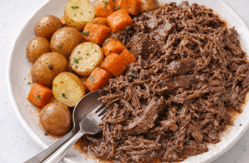 Beef stew with tender shredded beef, baby potatoes, carrots, and herbs on a white plate.